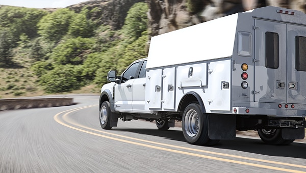 Ford Super Duty Chasis blanca con carrocería de servicio remolcando en una carretera de montaña con curvas.